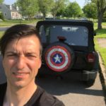 A man standing in front of a jeep with captain america 's shield on it.