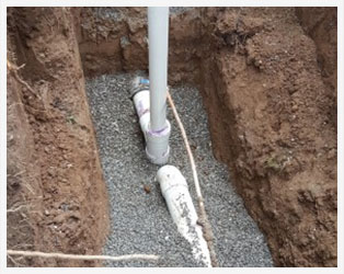 A pipe laying in the ground with wires plugged into it.